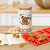 Dog treat canister with a dog illustration, red silicone mold, and dog treats on a wooden surface.